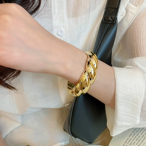 Detail of chunky gold twisted bangle with high-gloss finish worn on wrist over a white shirt