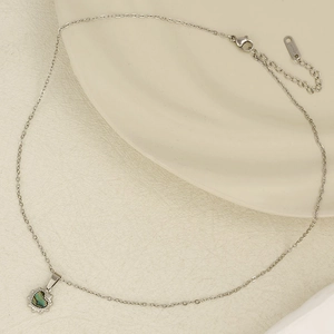 Detailed view of silver heart pendant with iridescent inlay on a textured beige surface