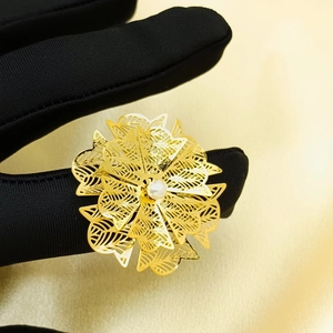 Close-up of gold hollow flower ring with pearl on black glove and satin background