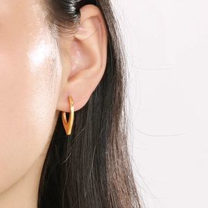 Nahaufnahme eines goldenen geometrischen V-Ohrrings, getragen in minimalistischem Stil
