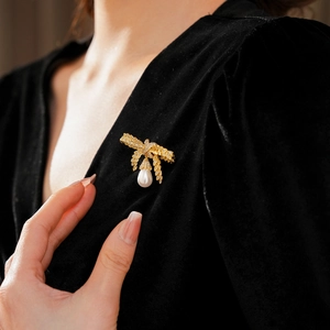 Gros plan d'une broche nœud dorée avec perles et zircons sur vêtement noir