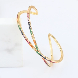Golden crossover cuff bracelet with rainbow cubic zirconia on white marble base