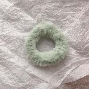 Detail of soft light green plush faux rabbit fur scrunchie with fluffy texture on white base