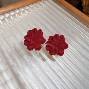Macro view of velvet-textured red flower earrings on a striped glass surface