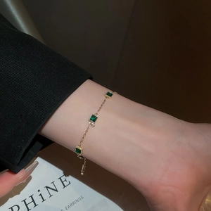Gros plan d'un bracelet doré avec pierres d'émeraude carrées au poignet d'une femme