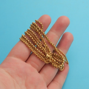 Detail of a shiny gold-plated square box chain necklace held in hand against blue background