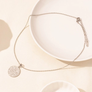 Macro shot of a round silver stainless steel pendant necklace on a minimalist ceramic plate