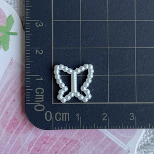 Detailed view of white pearl resin bow craft bead measured with ruler for DIY hair accessories