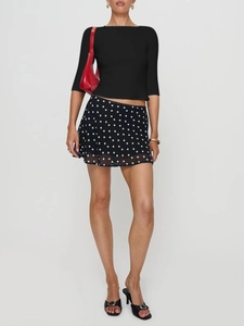 Detail of slim black long sleeve top paired with a polka dot chiffon mini skirt and red bag