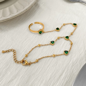 Close-up of gold chain finger bracelet with green heart gemstone on textured surface