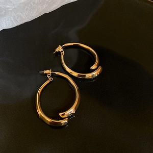 Macro detail of golden irregular twist hoop earrings on a reflective black surface