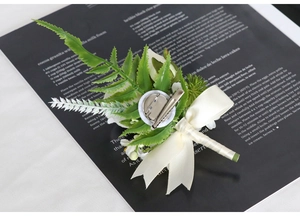 Detail of white rose boutonniere featuring silk petals, green fern leaves and metal pin back