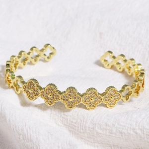 Détail d'un bracelet trèfle doré avec zircons sertis sur un tissu en lin blanc