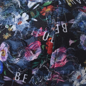 Detail of distressed denim fabric with floral lace patterns and frayed edge embroidery