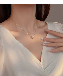 Close-up of a round pink shell pearl pendant on a delicate gold-tone chain necklace