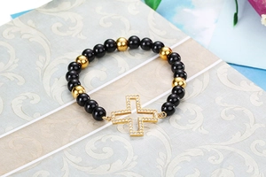 Close-up of black and gold beaded elastic bracelet featuring a large cross charm