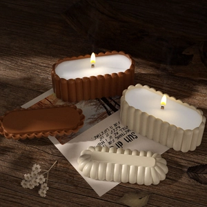 Close-up of ribbed oval candle jar molds in terracotta and beige with glowing lit wicks