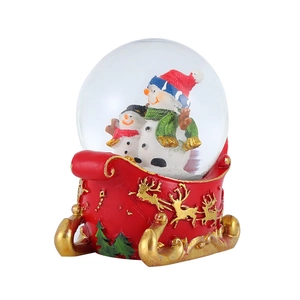 Close-up of Christmas crystal ball with snowmen inside and a red golden sleigh base
