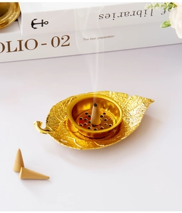 Detailed view of a gold leaf-shaped metal incense burner with a burning cone on white backdrop