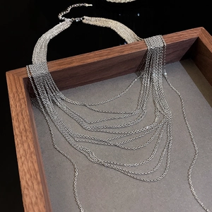 Detail of silver multi-layer geometric chain necklace on dark wooden tray display