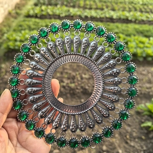 Close-up of a silver vintage round wall decor piece with green faceted gemstones