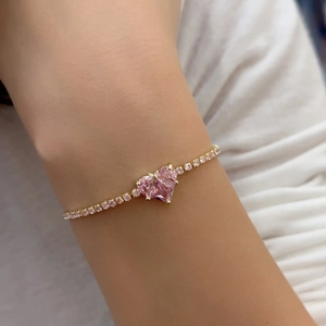 Macro detail of a gold chain bracelet featuring a large pink heart-shaped zircon stone