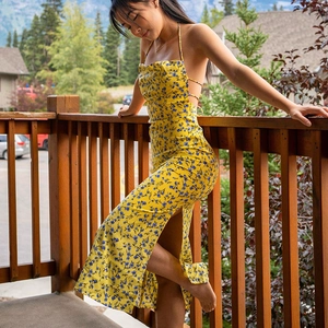 Detail showing the yellow floral dress with halter neck and side split on a sunlit balcony