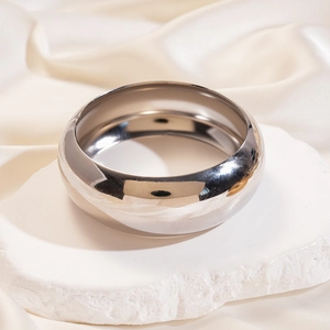 Detail of silver polished thick metal bangle on stone pedestal with satin fabric