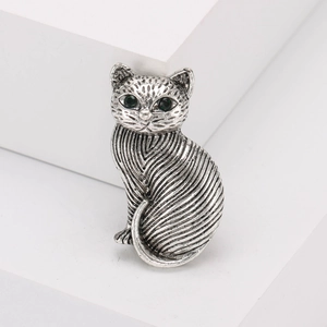 Vintage silver cat brooch with green gemstone eyes on minimalist white background