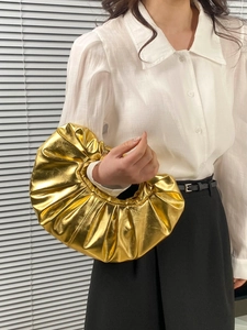 Metallic gold cloud bag in pleated PU leather held by a model against a grey background