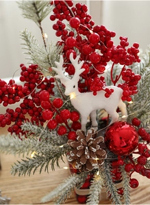 Close-up of Christmas decoration with pine needles, red berries, and white deer statue