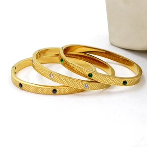 Detail of three gold titanium steel bangles with snake scale patterns and colored stones