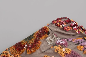Macro shot of colorful floral embroidery and sparkling sequins on black mesh dress fabric