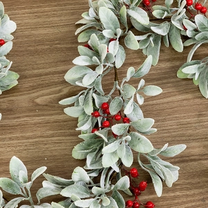 Artificial Christmas garland with frosted rabbit ear leaves and red berries on wood