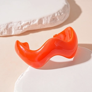 Detail of a bright orange wavy acrylic open cuff bracelet on a white textured stone