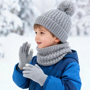 Close-up of grey knit hat with fur pompom, scarf and gloves set in snowy outdoor setting