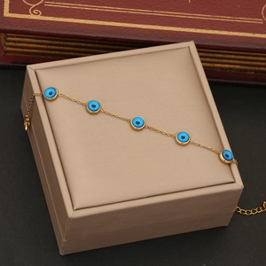 Gold evil eye bracelet with five blue circular charms displayed on a beige jewelry box