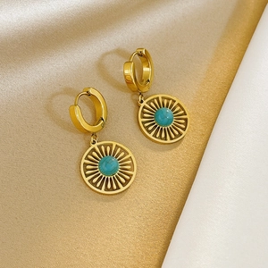 Golden sunburst earrings with turquoise stone on a minimalist reflective backdrop