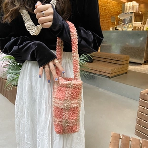 Plush pink and beige checkerboard handbag held by a model in a cozy cafe setting