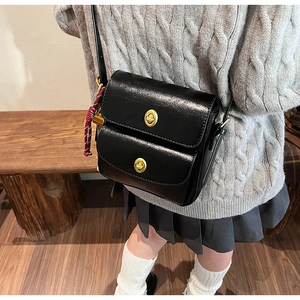 Detail of black crossbody bag with double gold twist locks and glossy leather finish