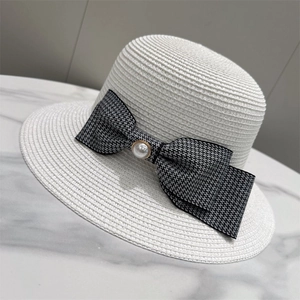 Detail of white straw hat featuring houndstooth ribbon and a gold-edged pearl button