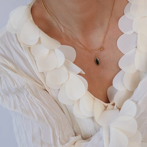Détail d'un collier double couche doré avec pendentif ovale noir porté par un mannequin