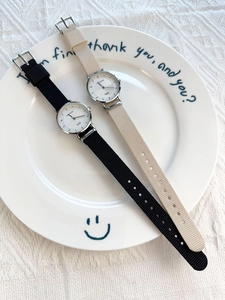 Detail shot of two minimalist nylon strap quartz watches displayed on a ceramic plate