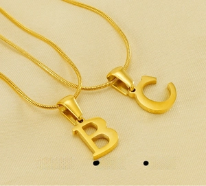 Macro detail of polished stainless steel gold B and C letter pendants on a snake bone chain
