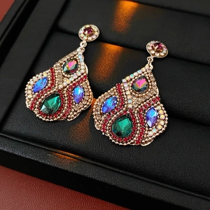 Détail de boucles d'oreilles vintage dorées avec pierres colorées et micro-strass rouges