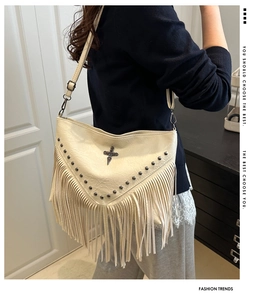 Detail view of beige studded PU leather crossbody bag with tassel and cross emblem on model