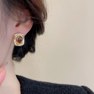 Close-up of a vintage rectangular gold stud earring with amber resin on a model ear