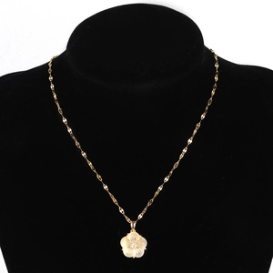 Macro shot of gold stainless steel necklace featuring a white shell flower pendant on black velvet