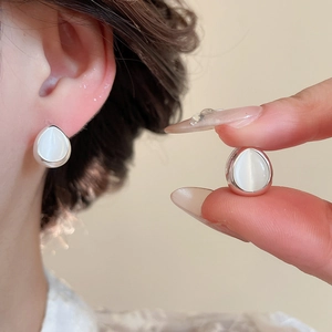 Macro shot of silver teardrop stud earrings with white cat-eye stones and polished metal edge
