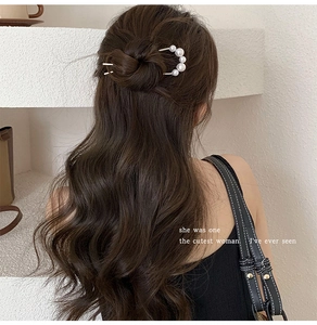 U-shaped hair pin with gradient white pearls securing a low bun hairstyle on wavy hair